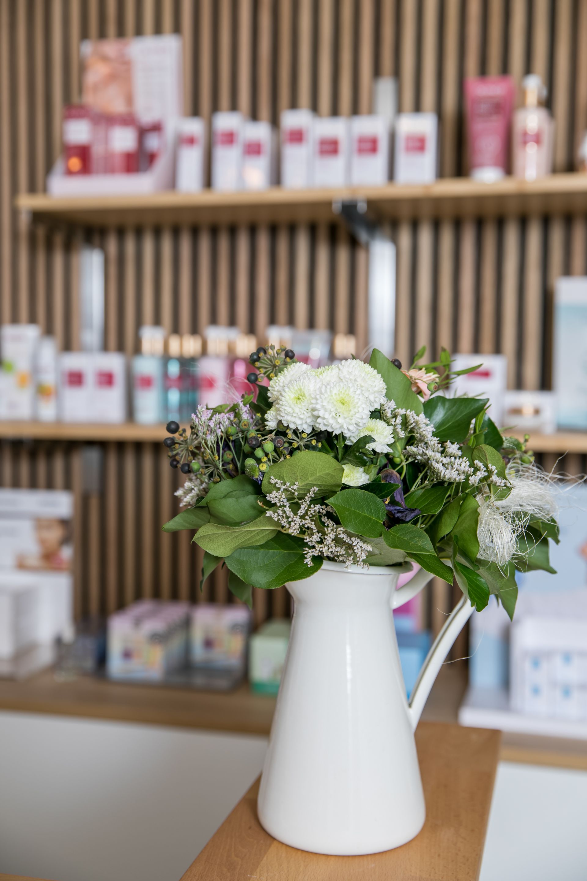 Weißer Krug mit Blumen in einem Schönheitssalon mit Hautpflegeprodukten in den Regalen.
