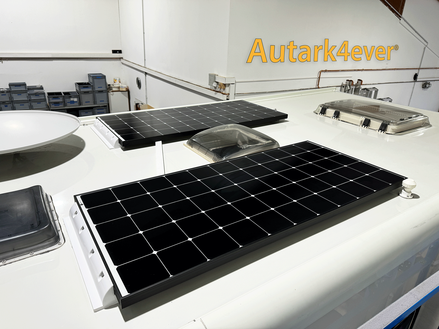Auf dem Dach eines Wohnmobils installierte Solarmodule. Weißer Rahmen um schwarze Module.