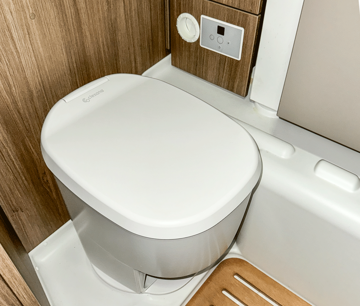 Eine tragbare Wohnmobiltoilette mit geschlossenem weißen Deckel in einem kleinen Badezimmer.