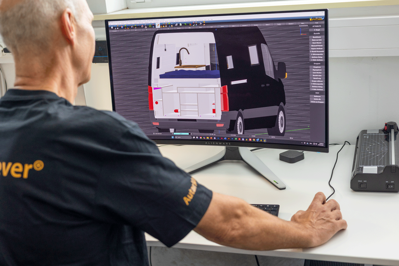 Mann entwirft am Computer an einem Schreibtisch die Innenausstattung eines Lieferwagens. Auf dem Bildschirm wird das Fahrzeugdesign in Weiß und Schwarz angezeigt.