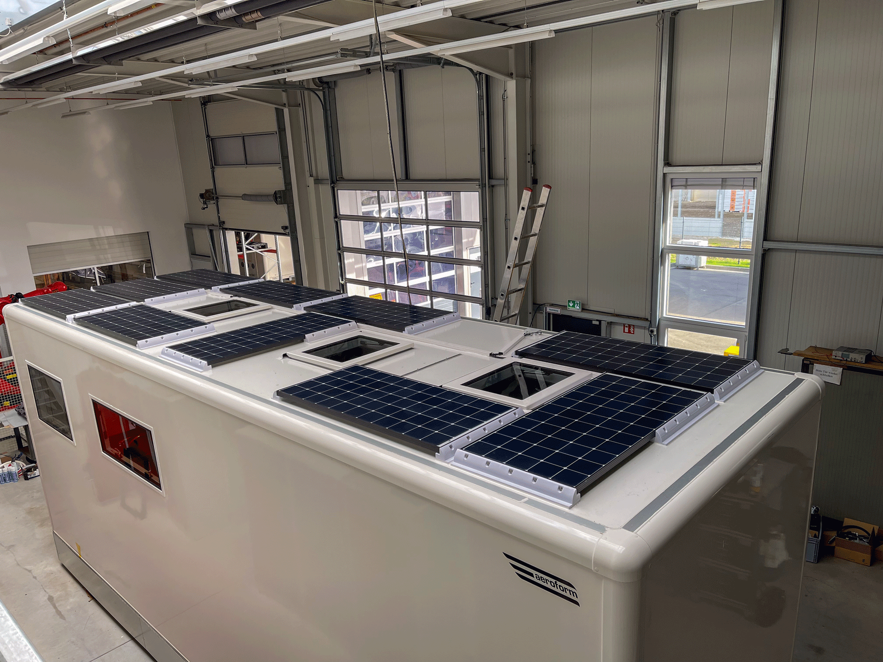 Solarmodule auf einem weißen Wohnmobildach in einer Garage, mit offenen Oberlichtern und sichtbarem Garagentor.