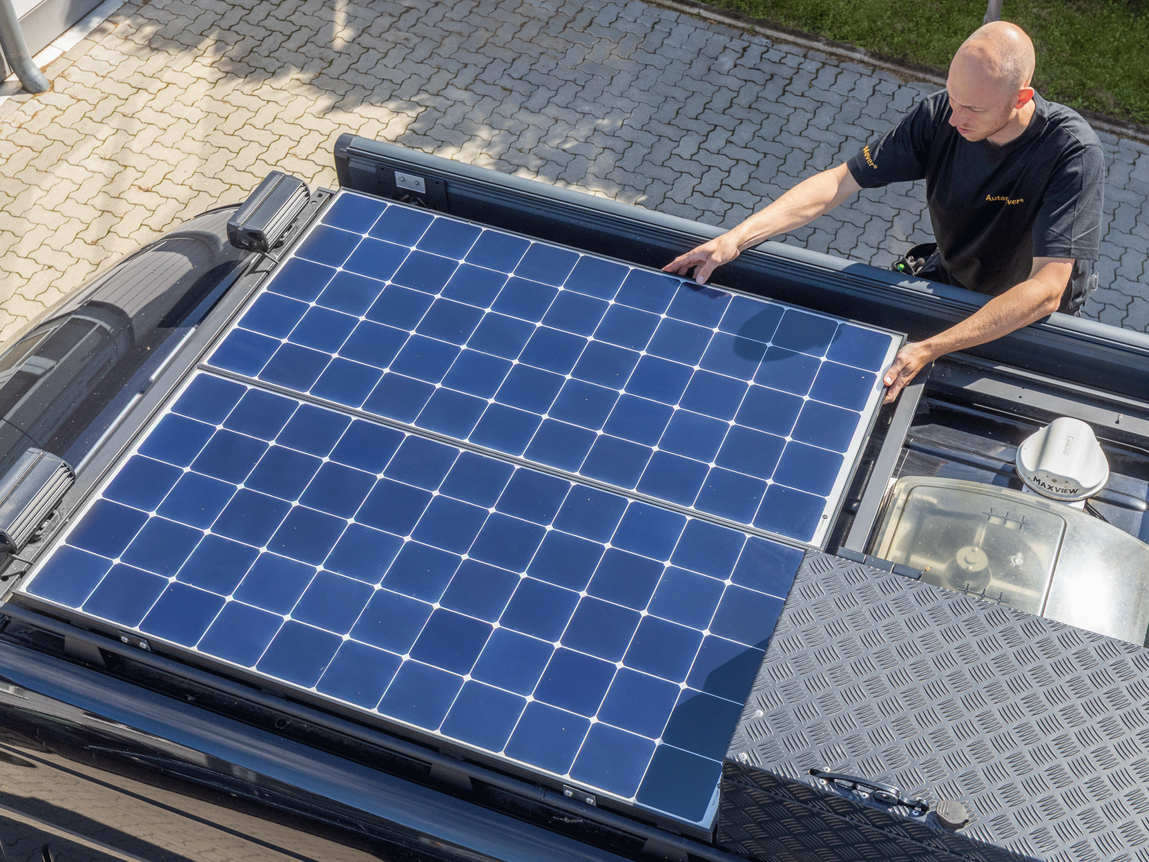 Mann installiert Solarmodule auf dem Dach eines Fahrzeugs. Blaue Module, sonnige Außenansicht.