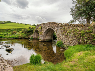 Vieux pont de pierre enjambant un ruisseau paisible dans un paysage champêtre verdoyant