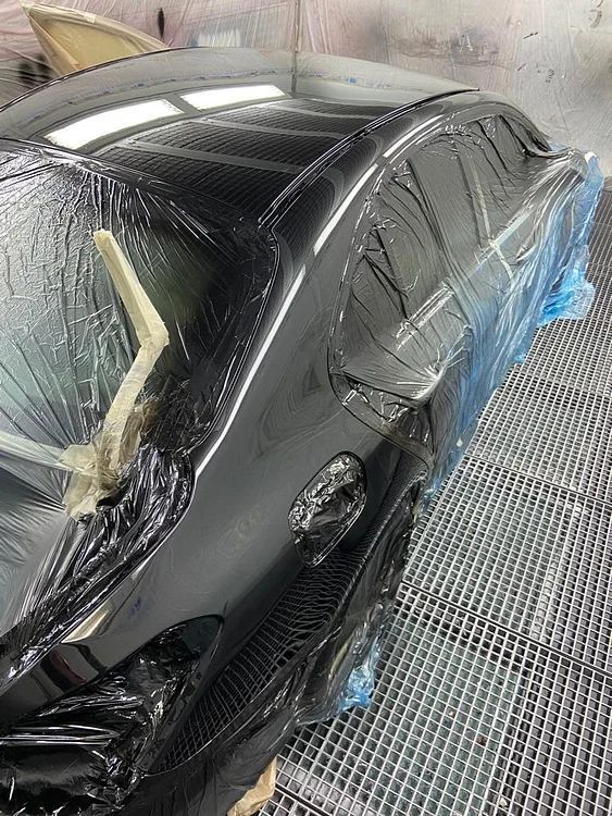 Ein schwarzes Auto ist in Plastik eingewickelt und steht in einer Lackierkabine.