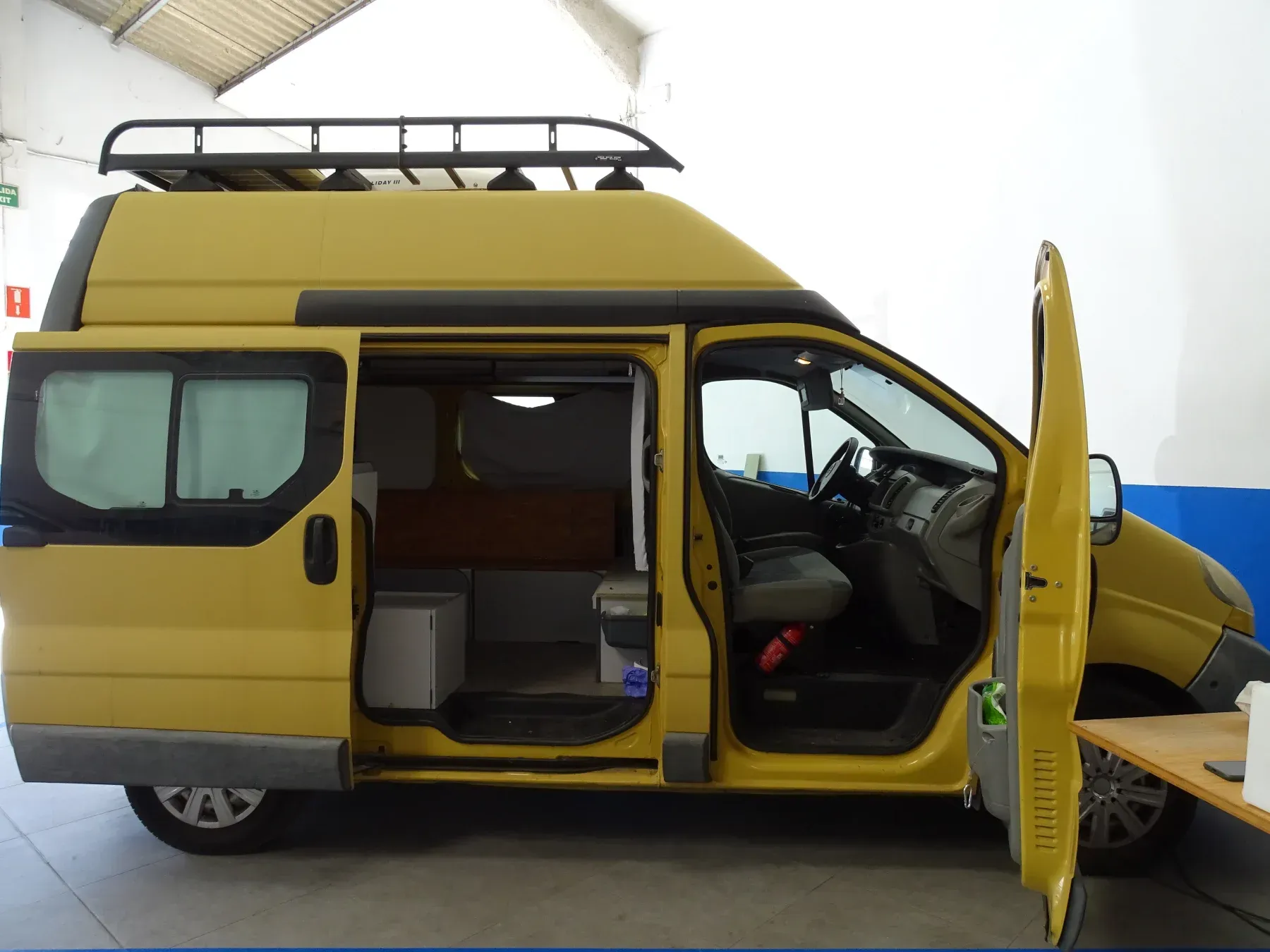 Furgoneta camper amarilla con puertas laterales y delanteras abiertas, baca, aparcada en interior.