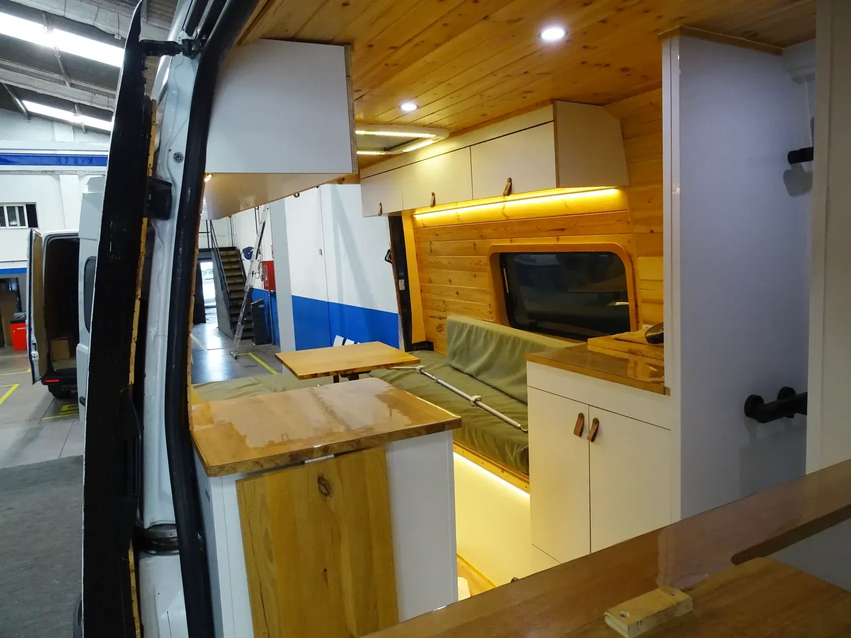 Interior de una furgoneta camper con paneles de madera, armarios y sofá.