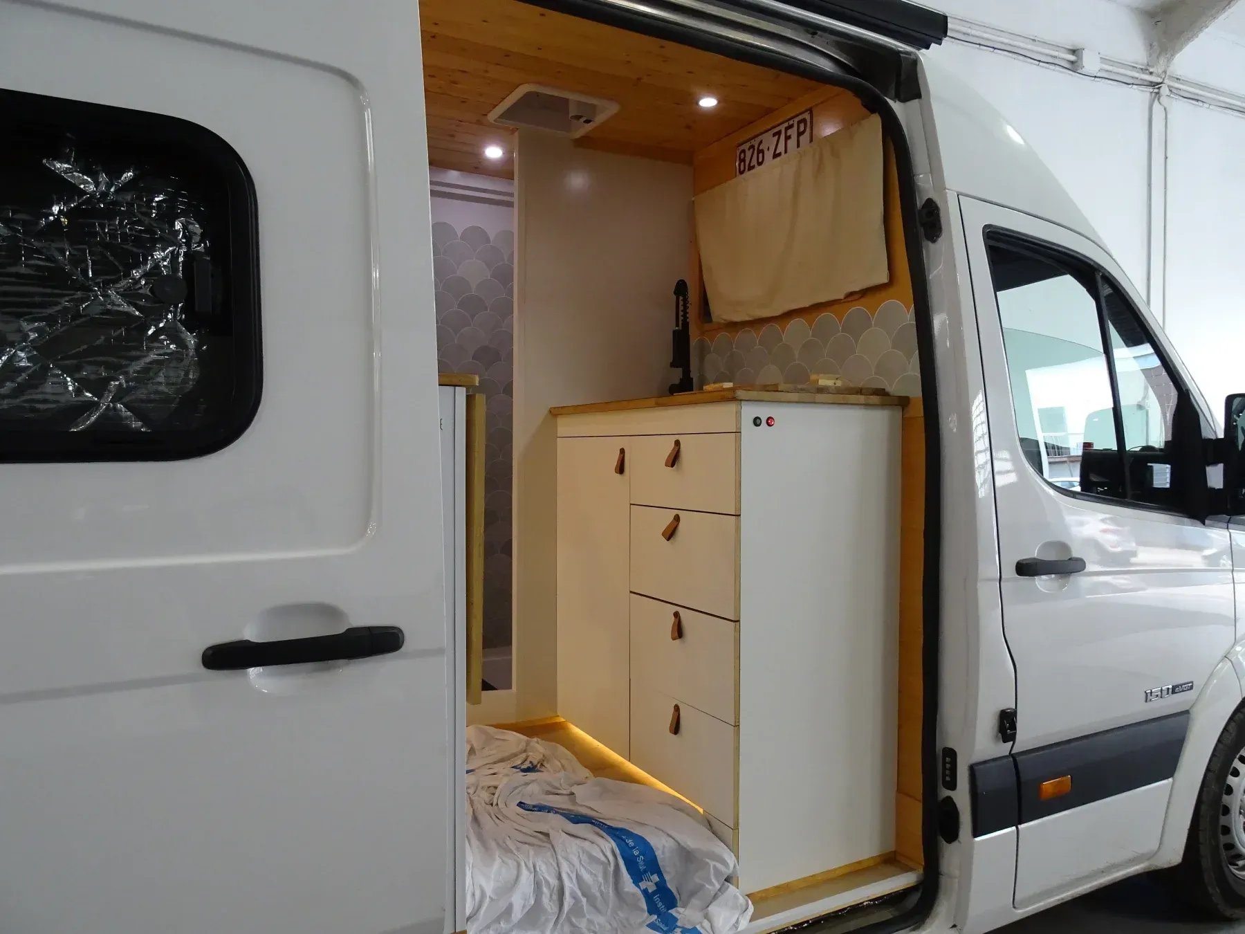 Interior de una furgoneta blanca donde se aprecia la cocina, los armarios