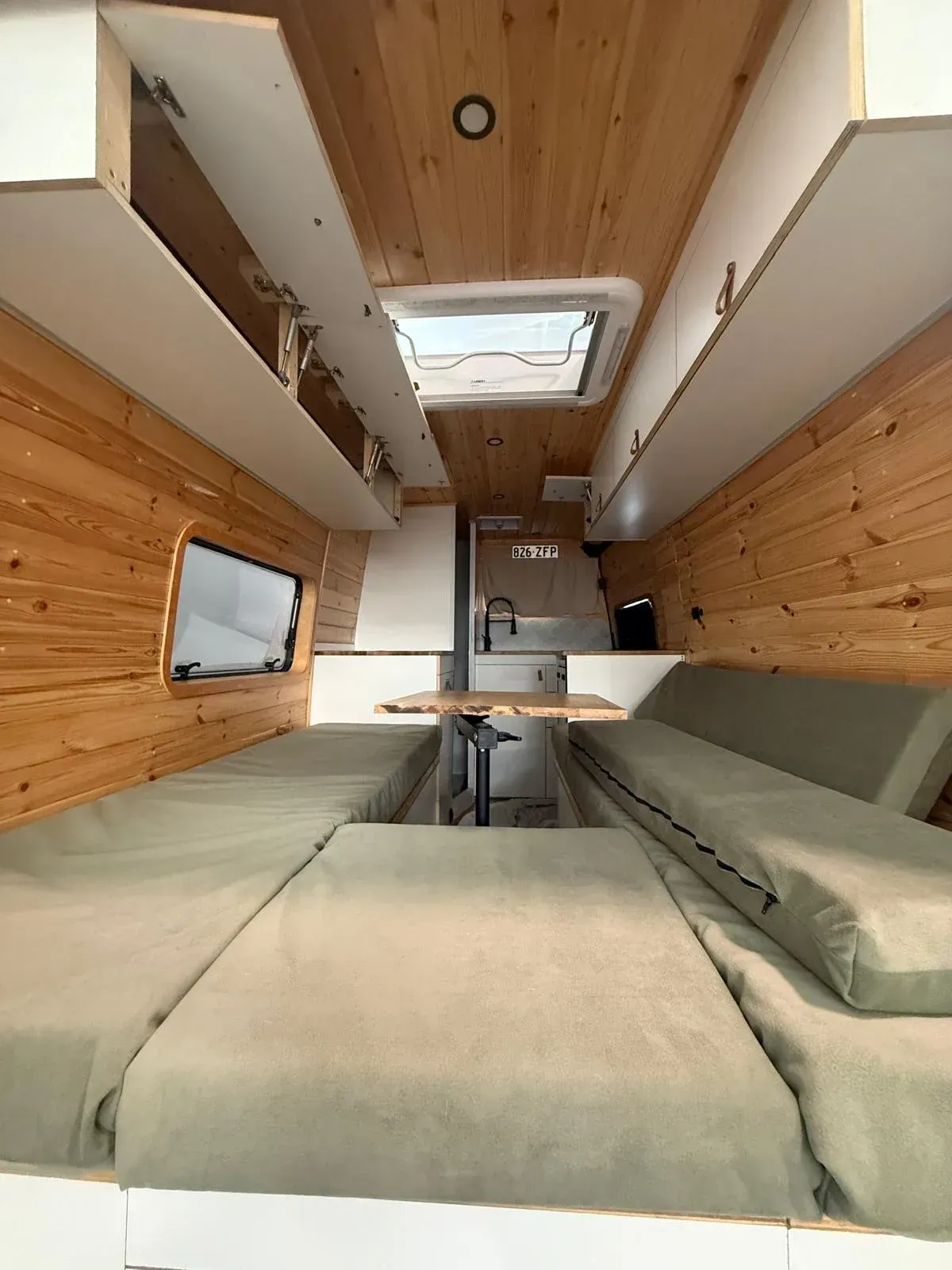 Vista interior de una autocaravana con paneles de madera, claraboya y cama/mesa convertible.