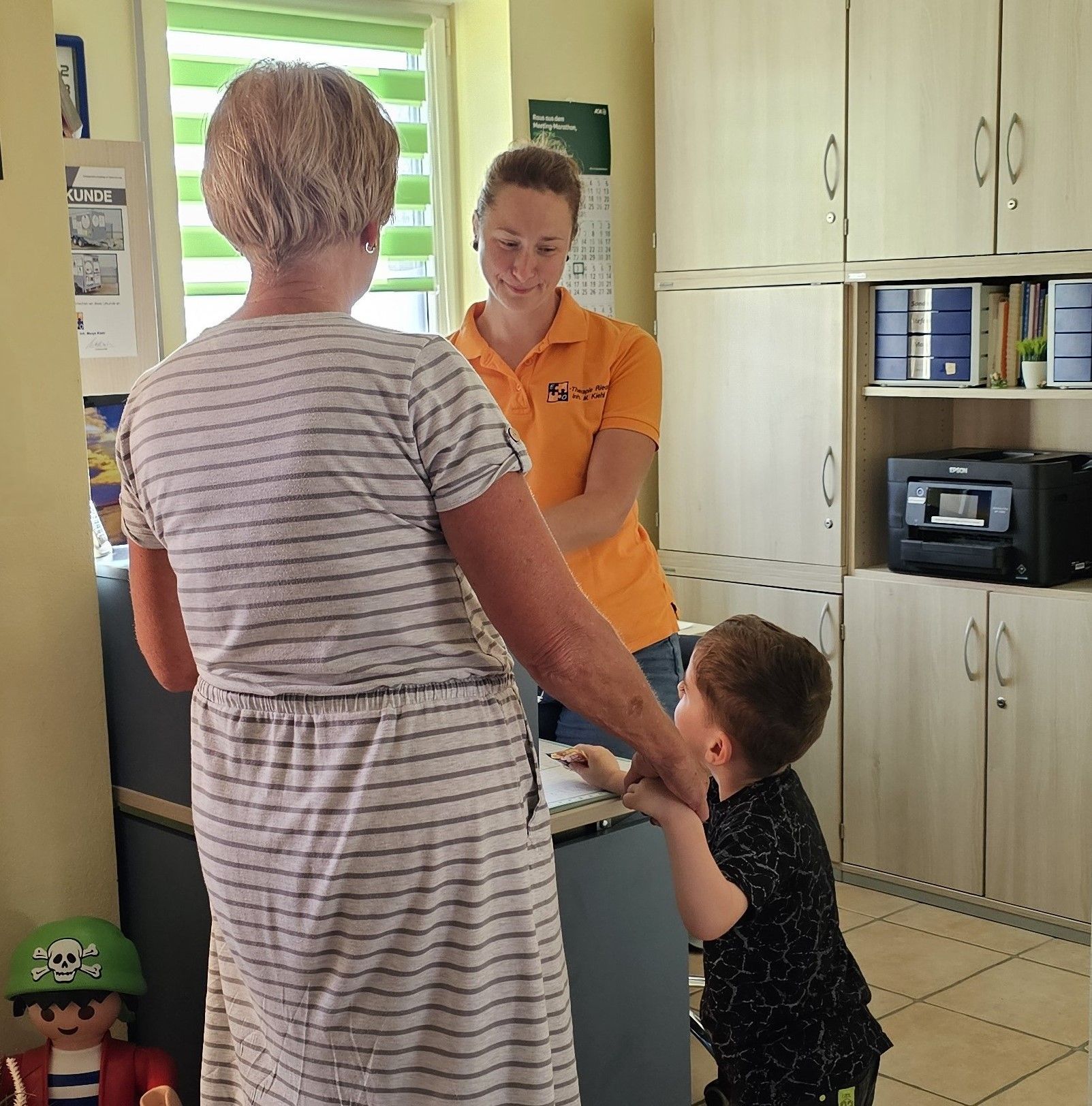 Gelbes Gebäude mit „Ergotherapie“-Schild, geparkter blauer Oldtimer, gepflasterte Auffahrt.