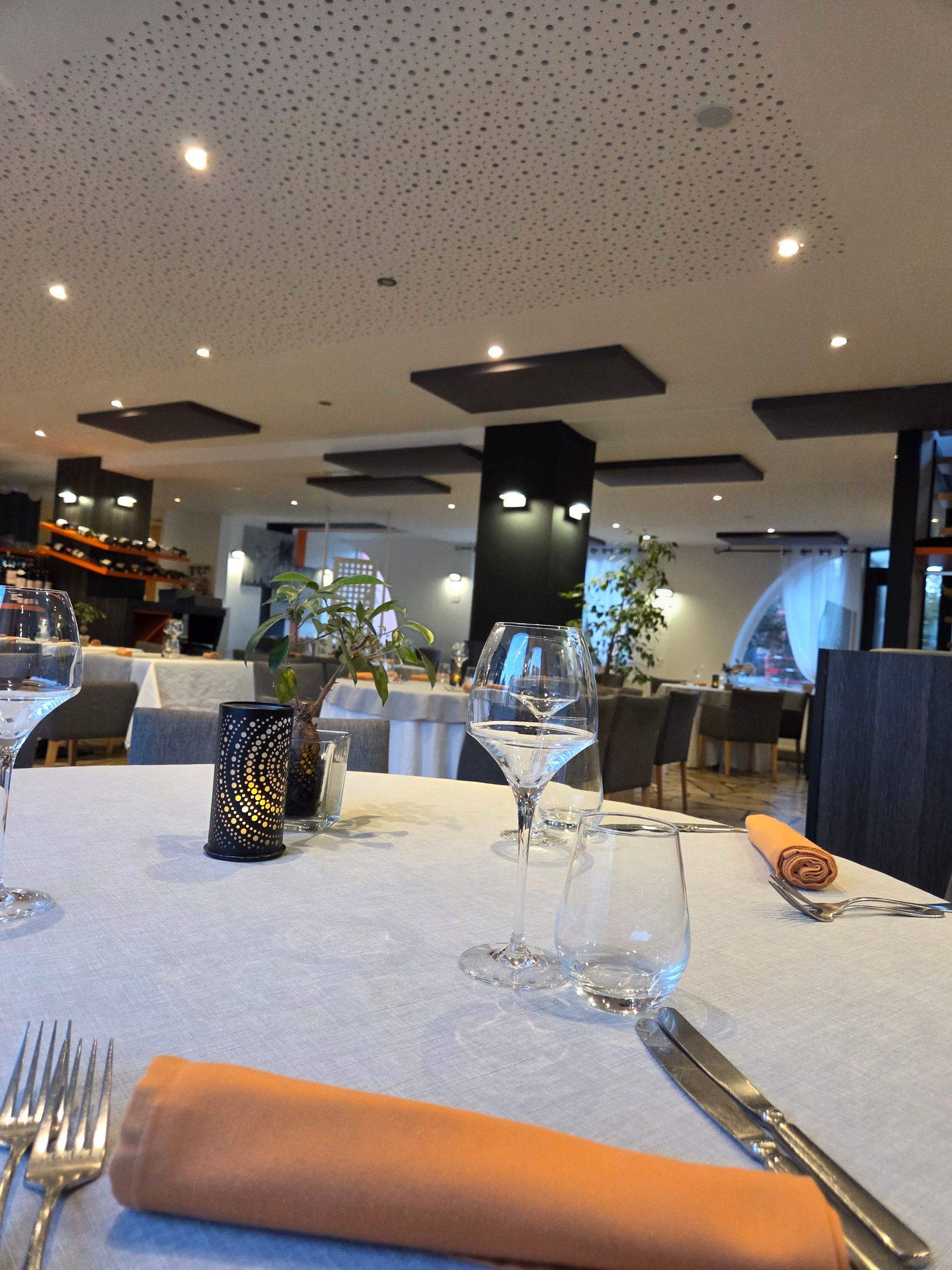 Vue intérieure d'un restaurant avec des tables recouvertes de nappes blanches et des chaises rembourrées gris foncé.