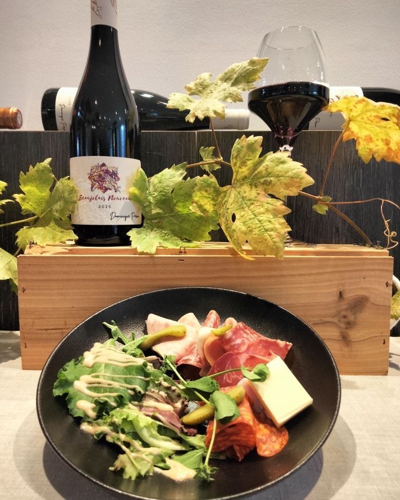 Une assiette de charcuterie et de salade est posée devant une caisse en bois contenant une bouteille de vin.