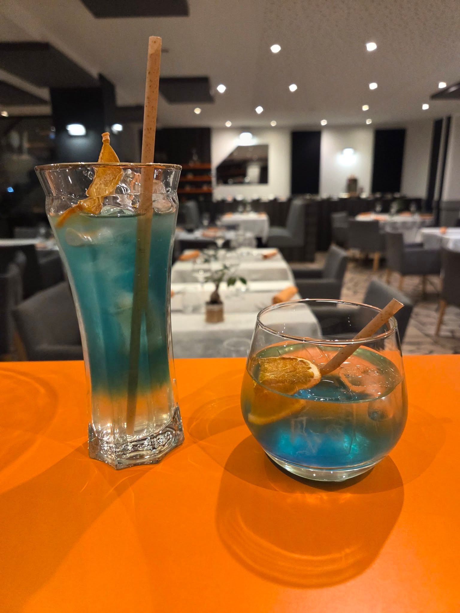 Deux cocktails bleus, garnis d'agrumes et accompagnés de pailles.