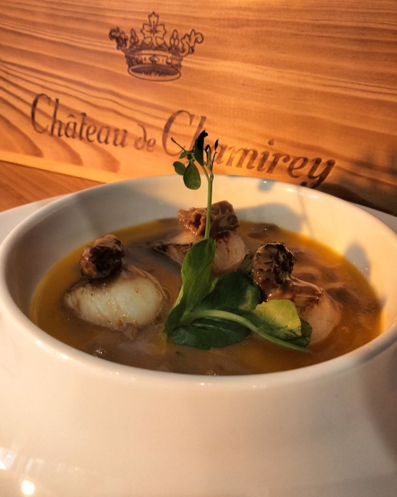 Un bol gastronomique de soupe aux pétoncles, aux légumes verts et aux champignons.