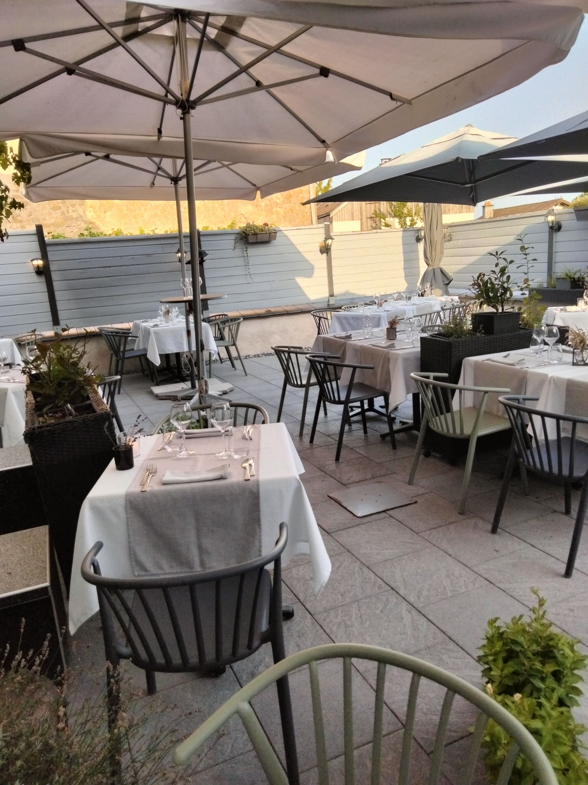 Une terrasse de restaurant ensoleillée en plein air, avec plusieurs tables dressées.