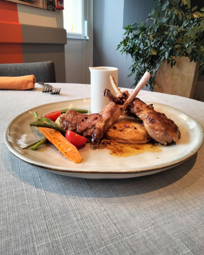 Une assiette composée de deux côtelettes d'agneau poêlées, de carottes rôties et de tomates cerises.