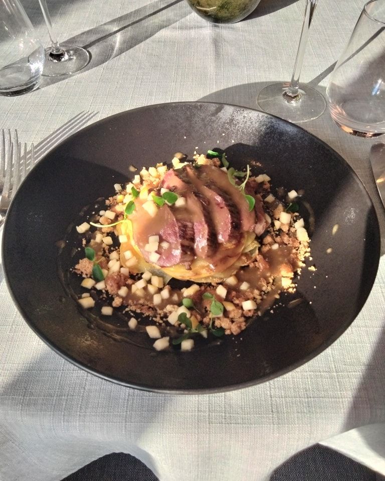 Une assiette de magret de canard mi-cuit, tranché et servi sur une purée de légumes avec des fruits coupés en dés.