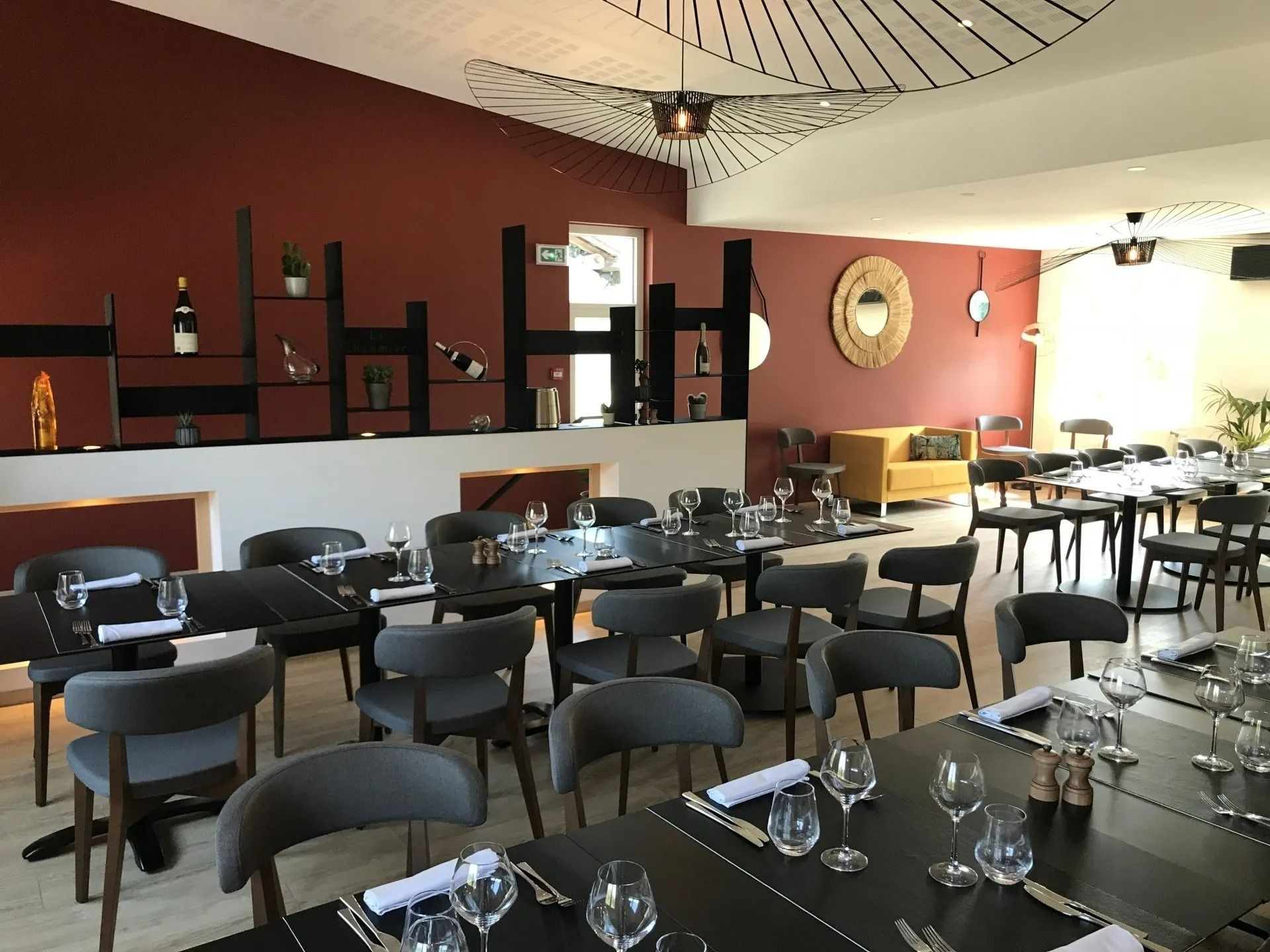 Une salle à manger de restaurant moderne avec des tables en bois foncé et des chaises grises, des murs rouges.