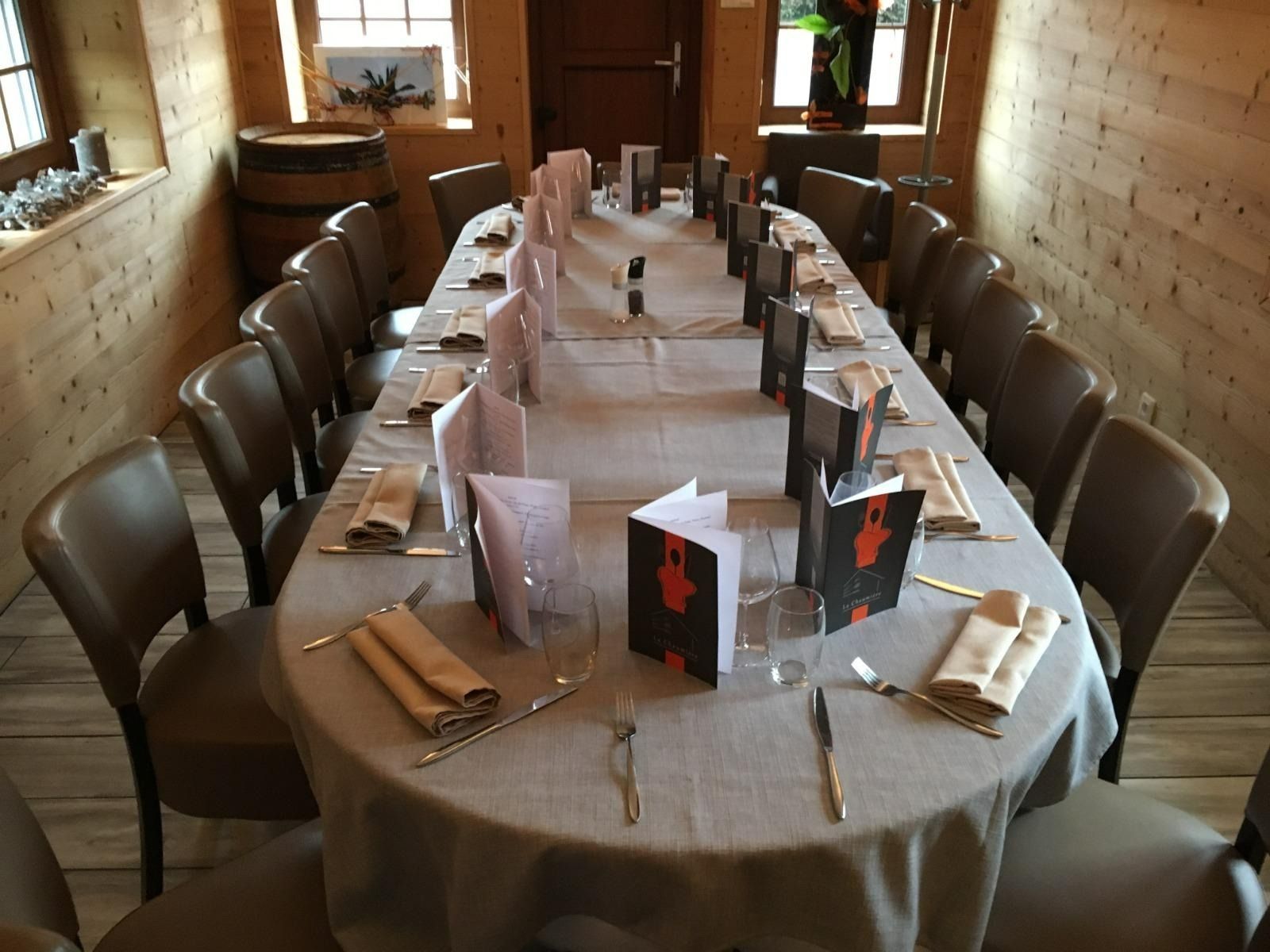 Dans une pièce rustique aux murs en bois, une table ovale en bois est dressée pour un dîner formel.