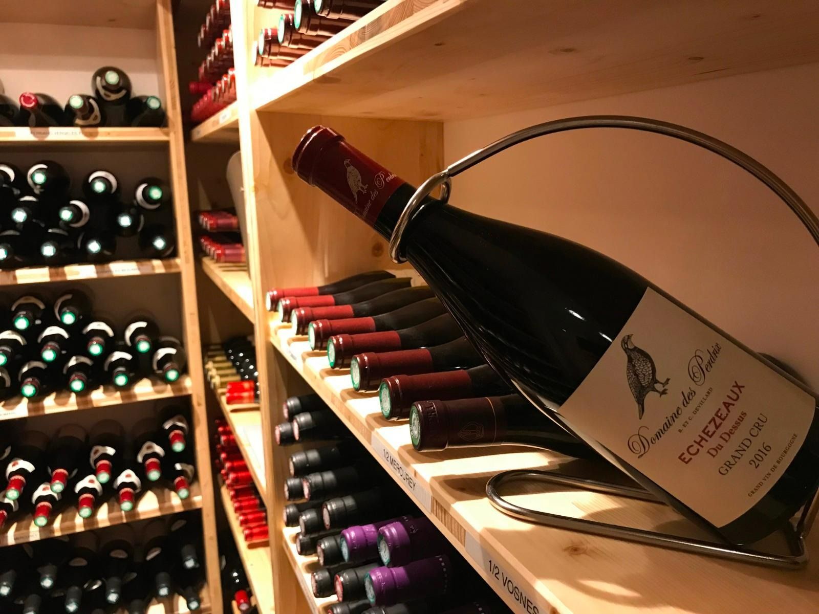 Une cave à vin dont les étagères regorgent de bouteilles, avec une bouteille d'Échezeaux posée sur un présentoir métallique.