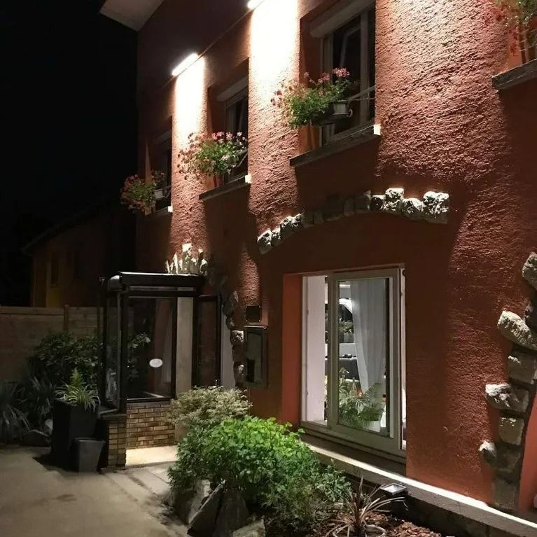 La nuit, la façade d'un bâtiment couleur pêche illuminée, avec des jardinières de fleurs aux fenêtres.