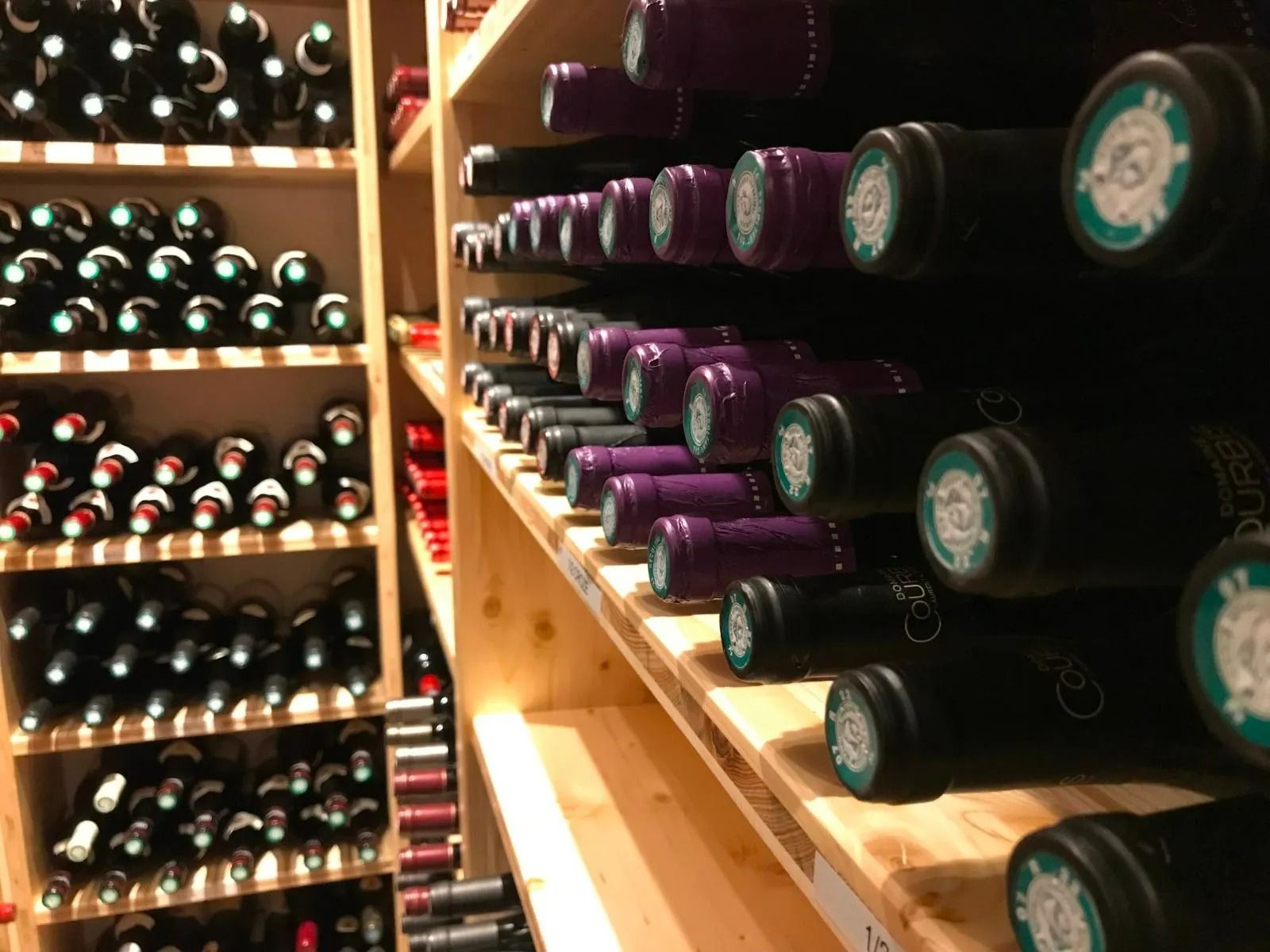 Des bouteilles de vin sont rangées sur des étagères en bois dans une cave faiblement éclairée.