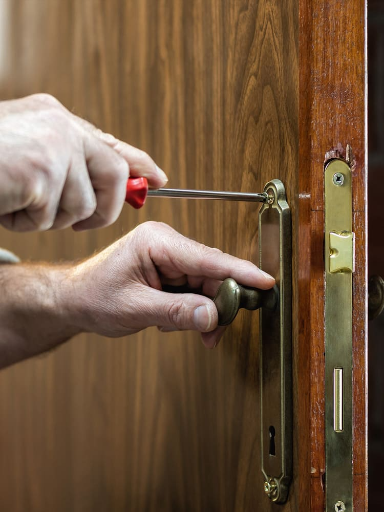 Un hombre está arreglando la manija de una puerta con un destornillador.