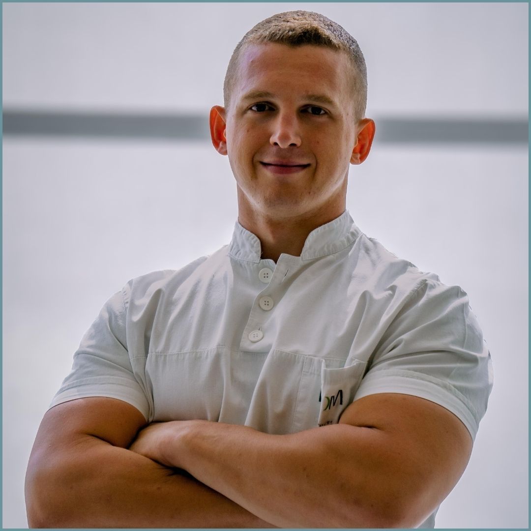 Uomo in uniforme bianca con le braccia incrociate, sorridente.