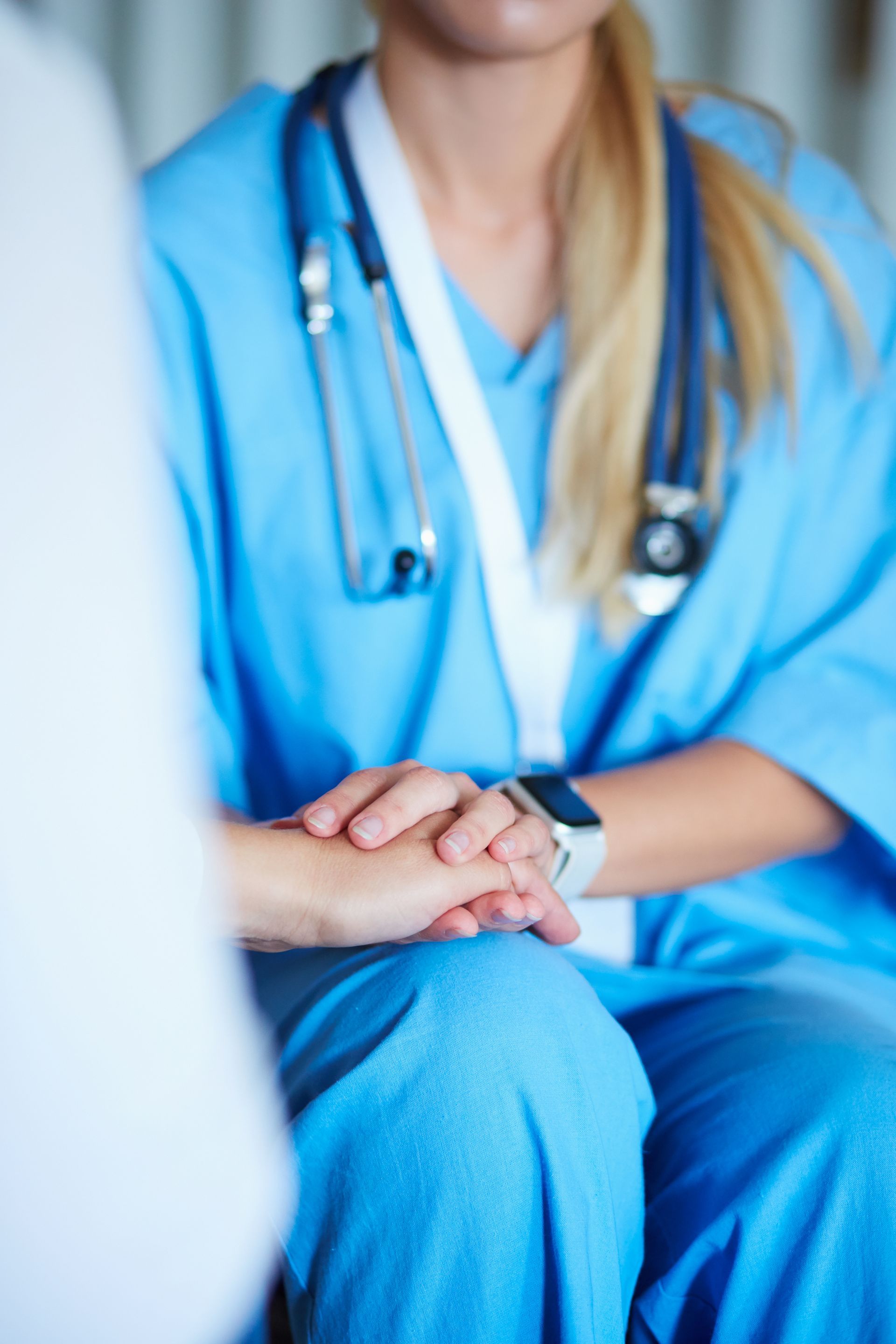 Un'infermiera bionda in camice blu e stetoscopio offre la sua assistenza professionale e tiene la mano di un paziente per confortarlo.