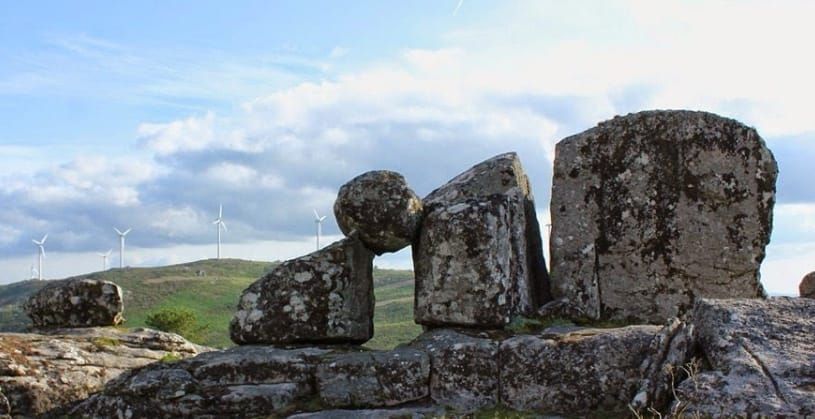 Un grupo de rocas situadas en la cima de una colina con turbinas eólicas al fondo.
