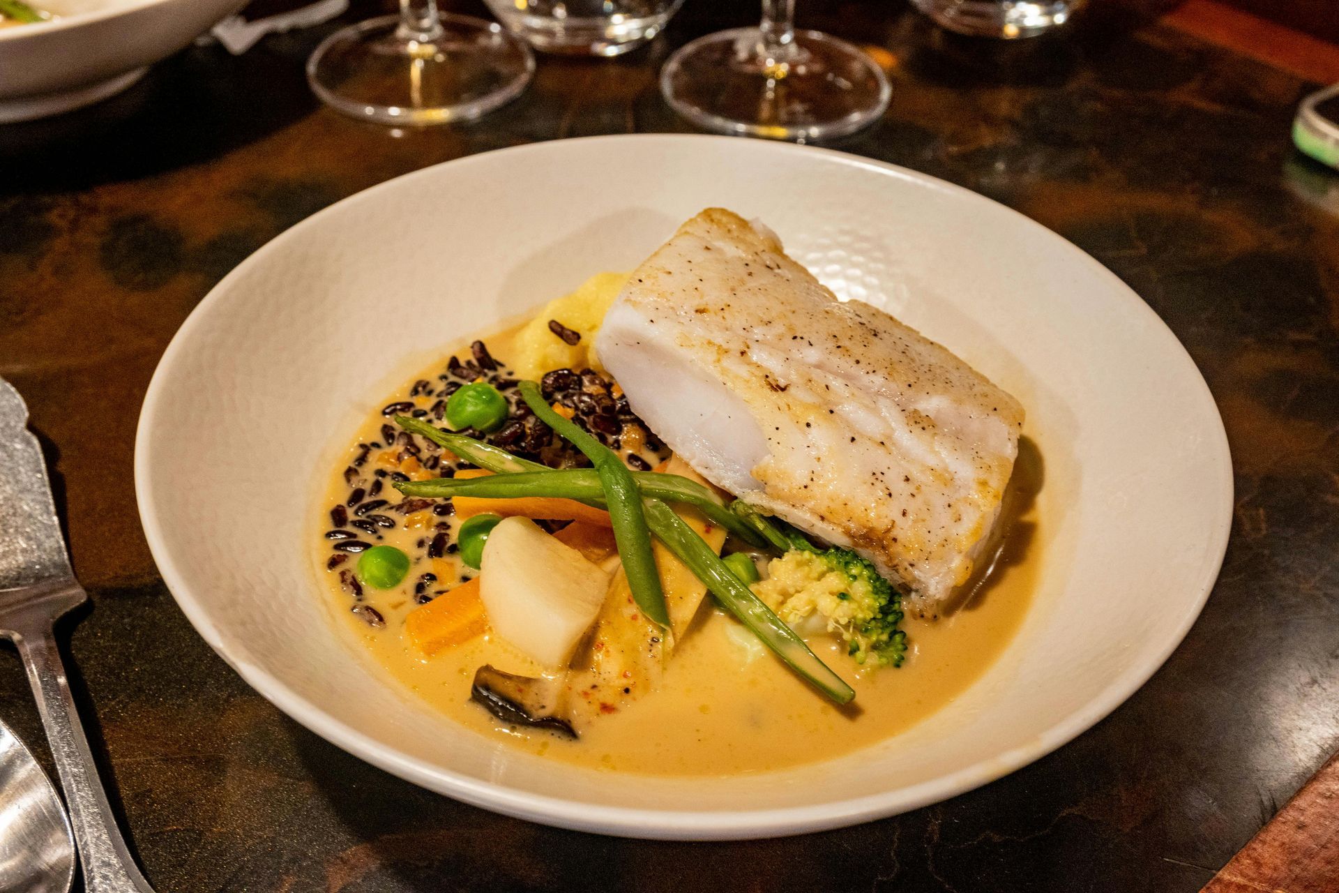 Un plato blanco cubierto con un trozo de pescado y verduras sobre una mesa.