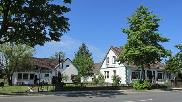 Weiße Gebäude mit dunklen Dächern und grünen Verzierungen, Bäume, blauer Himmel.