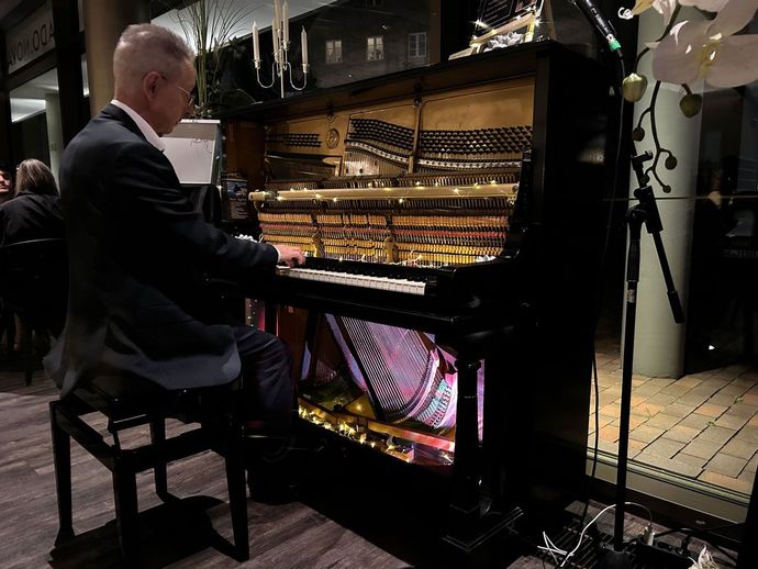 Ein Pianist spielt auf einem schwarzen Flügel, dessen Innenraum beleuchtet ist; ein Mikrofon steht daneben.