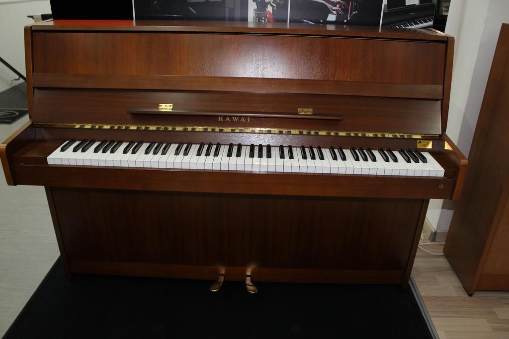 Aufrechtes Holzklavier mit offener Tastatur, Pedalen und Messingbeschlägen.