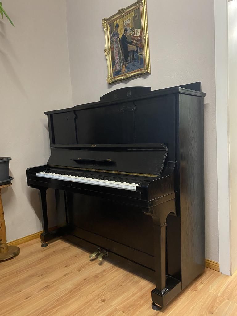 Ein schwarzes Klavier in einer Ecke, darüber ein goldgerahmtes Bild.