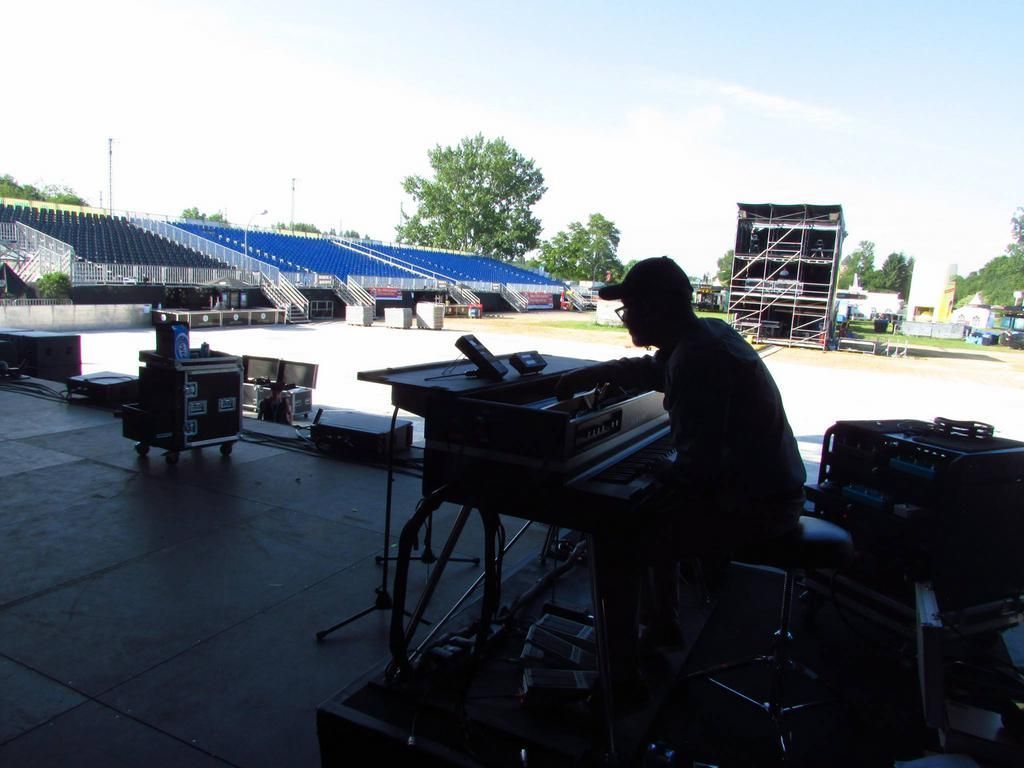 Eine Person spielt Keyboard auf der Bühne, im Hintergrund sind Stadionsitzplätze zu sehen.