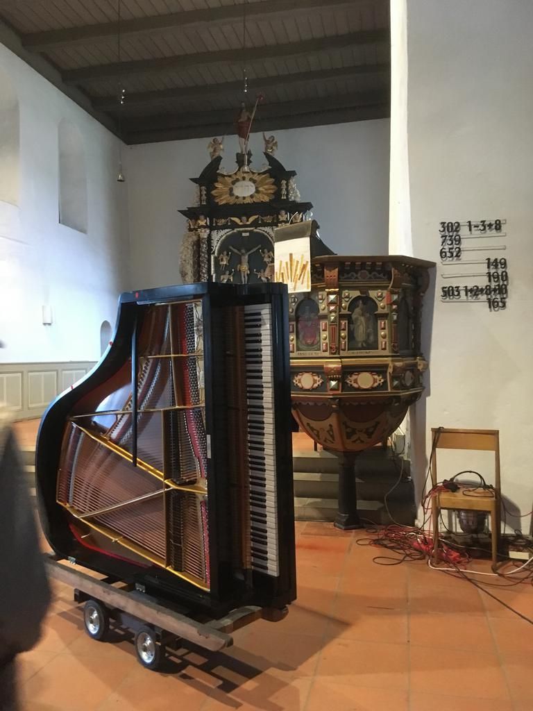 Ein Flügel auf Rollen in einer Kirche, in der Nähe einer verzierten Kanzel. Rote Kabel auf dem Boden.