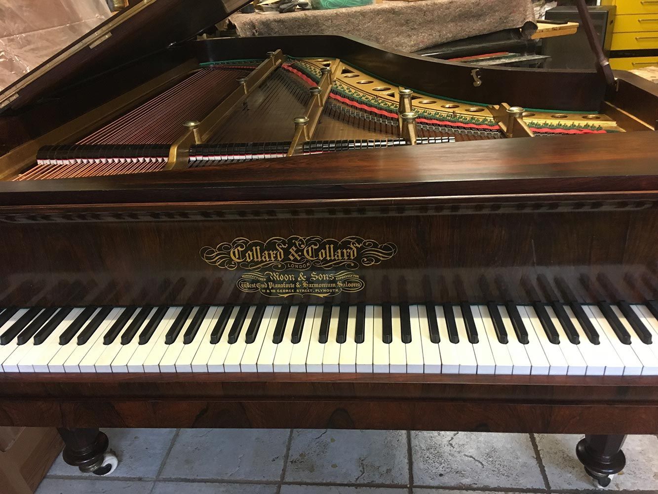 Braunes Klavier mit offenem Deckel, Tasten und kunstvoller goldener Beschriftung auf der Vorderseite.