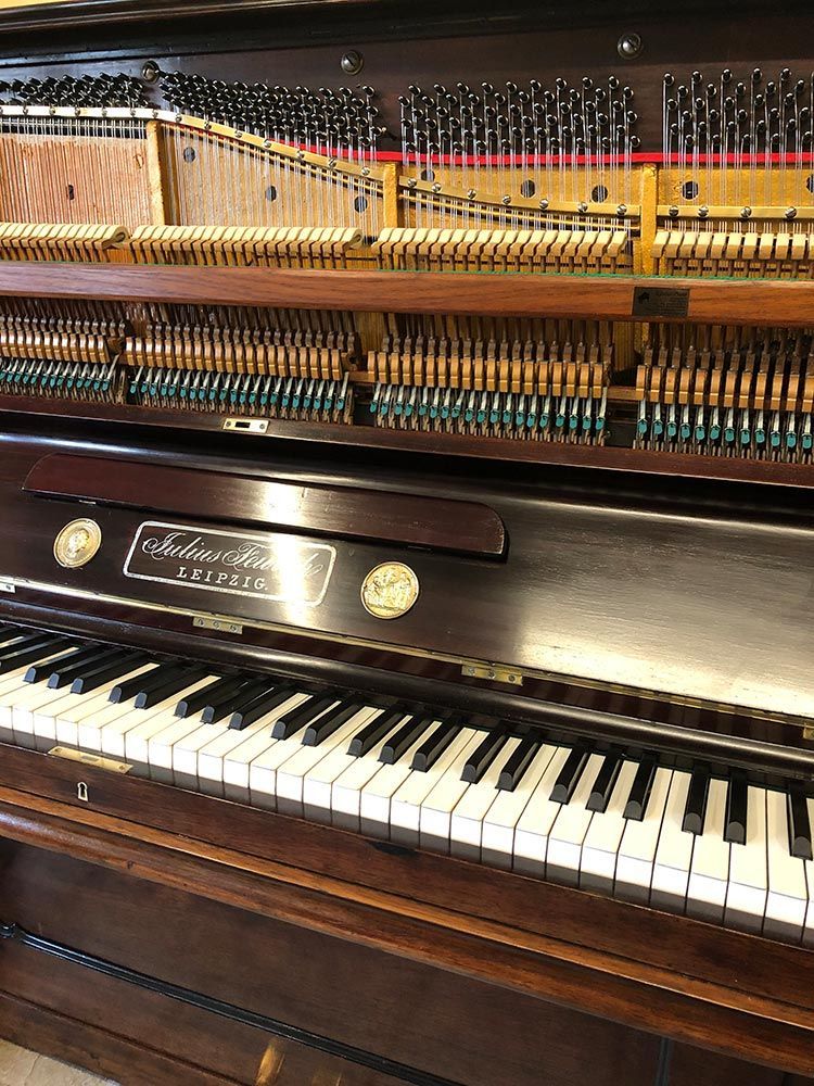 Aufrecht stehendes Klavier mit geöffnetem Deckel, der Saiten und Hämmer freigibt. Dunkles Holz mit elfenbeinfarbenen und schwarzen Tasten.