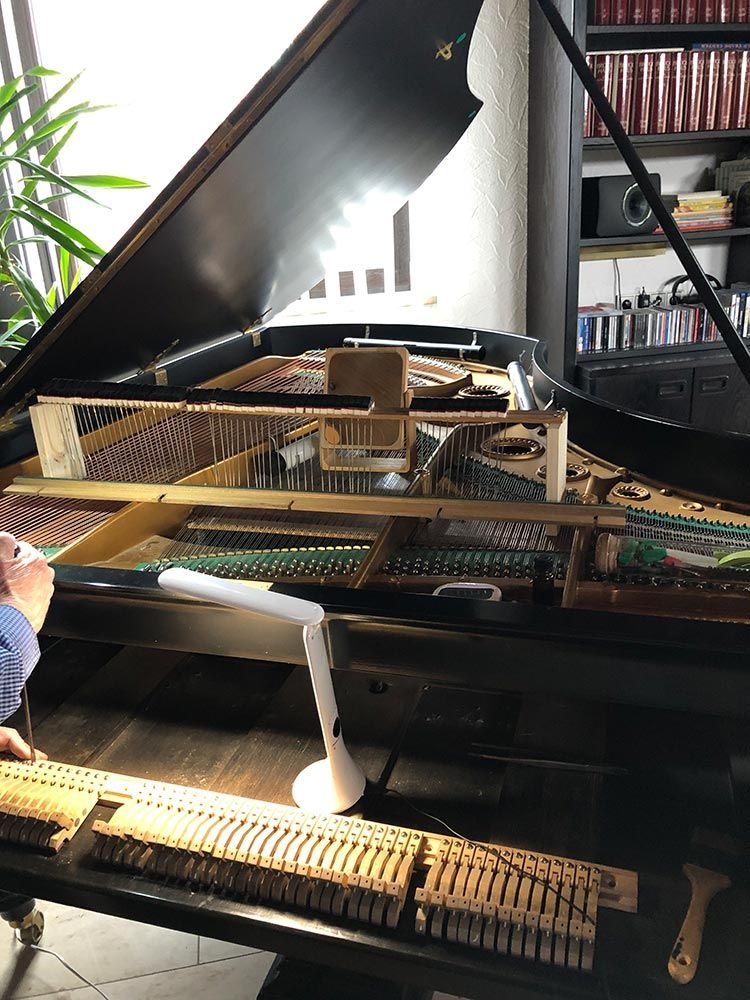 An einem Klavier wird gearbeitet, wobei die Tasten und die inneren Bauteile sichtbar sind und von einer Lampe beleuchtet werden.