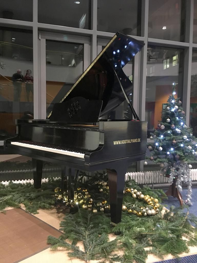 Ein schwarzer Flügel mit weihnachtlicher Dekoration, darunter ein Weihnachtsbaum, in der Eingangshalle eines Gebäudes.