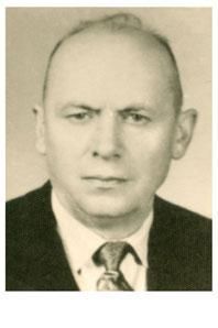 Mann im dunklen Anzug, weißem Hemd und Krawatte; ernster Gesichtsausdruck.