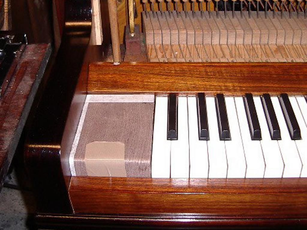 Nahaufnahme einer Klaviertastatur. Braunes Holz, weiße und schwarze Tasten, Reparaturklebeband ist sichtbar.