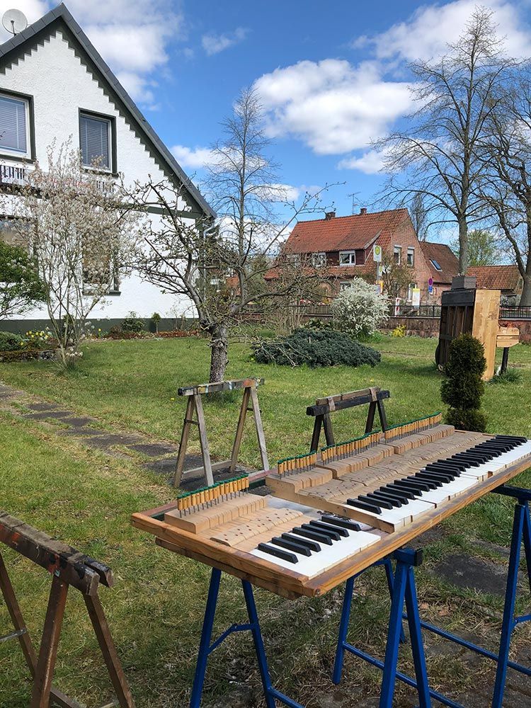 Eine Klaviertastatur auf Sägeböcken in einem Hof, im Hintergrund ein Haus. Strahlend sonniger Tag.
