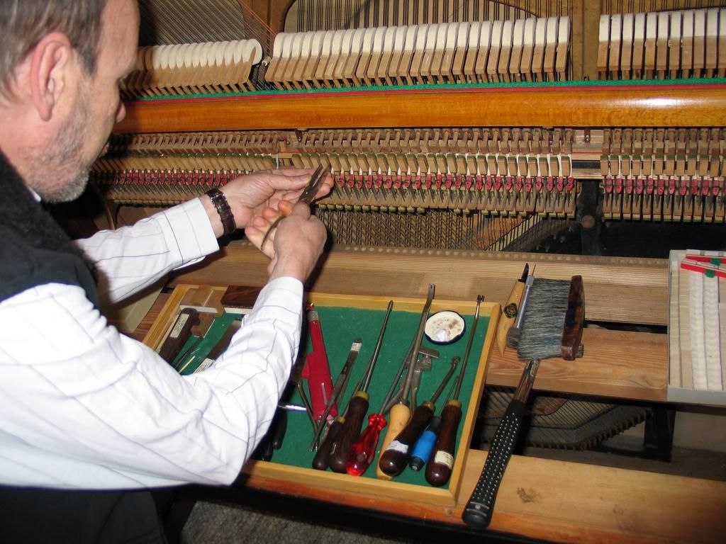 Eine Person arbeitet mit Werkzeug an der inneren Mechanik eines Klaviers. Das Werkzeug ist auf einem grünen Filztablett angeordnet.