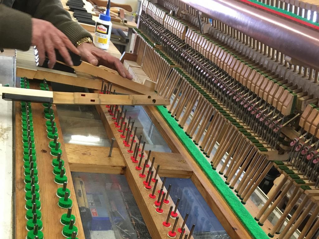 Eine Person arbeitet an der Klaviermechanik; Holzrahmen, Hämmer, Dämpfer und Saiten sind sichtbar.