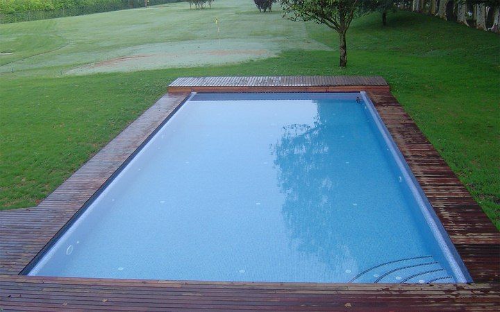Una gran piscina con terraza de madera rodeada de césped y árboles.