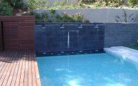 Una piscina con cascada y terraza de madera.