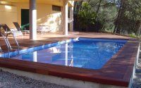 Una gran piscina está situada encima de una terraza de madera al lado de una casa.