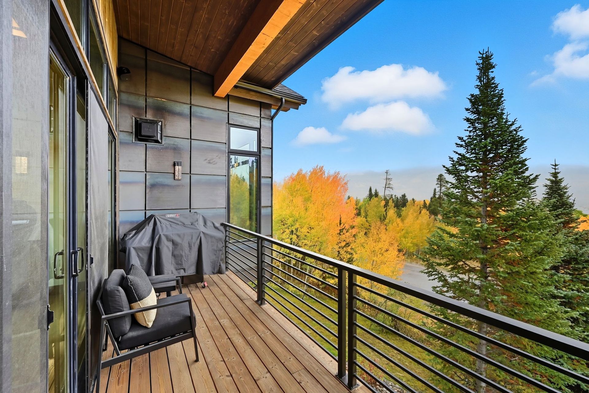 Balcony with grill, chair, and view of colorful autumn trees and sky.