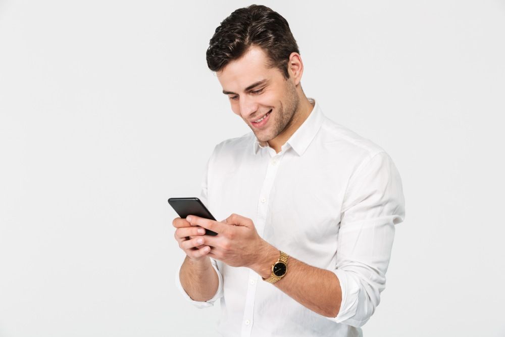 Man in white shirt smiling while looking at a smartphone, set against a white background.